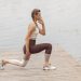 A woman performs lunges on a lakeside wooden deck, showcasing a fit lifestyle outdoors.
