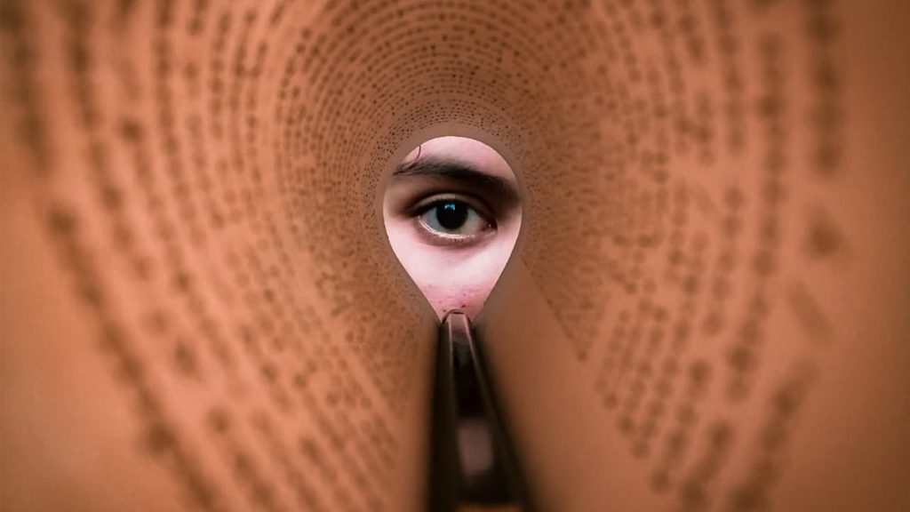 A person's eye looking through a rolled book page, creating a unique viewpoint.