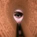 A person's eye looking through a rolled book page, creating a unique viewpoint.